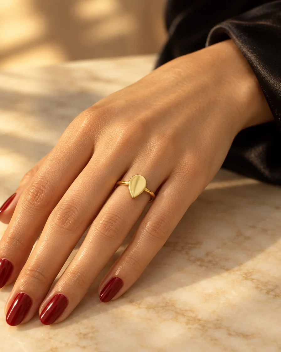 18K gold pear signet ring worn on the ring finger, hand resting on marble