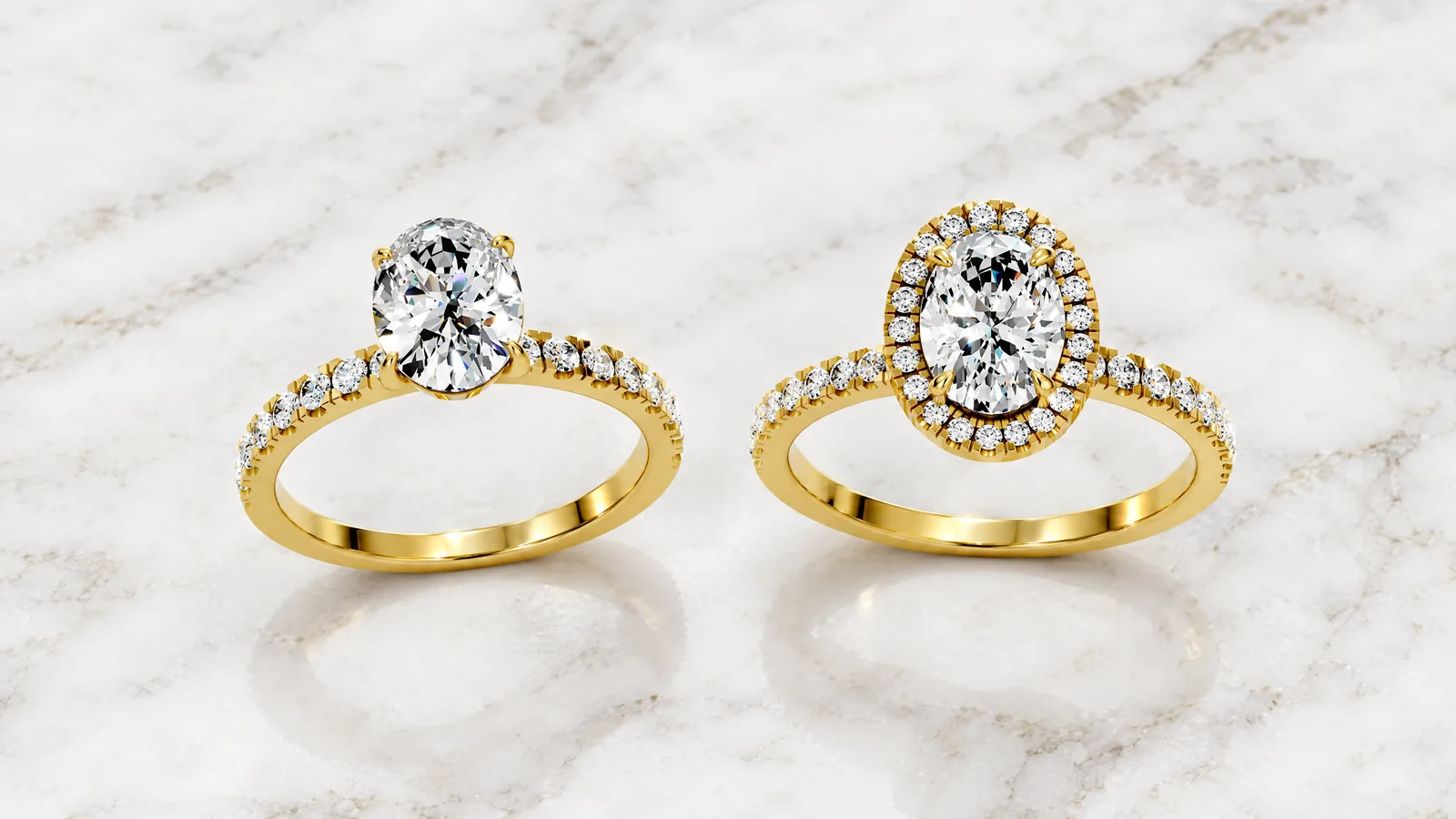 Two yellow gold oval diamond rings side by side on white marble: a solitaire with a pavé band and an oval halo ring whose centre diamond is the same size
