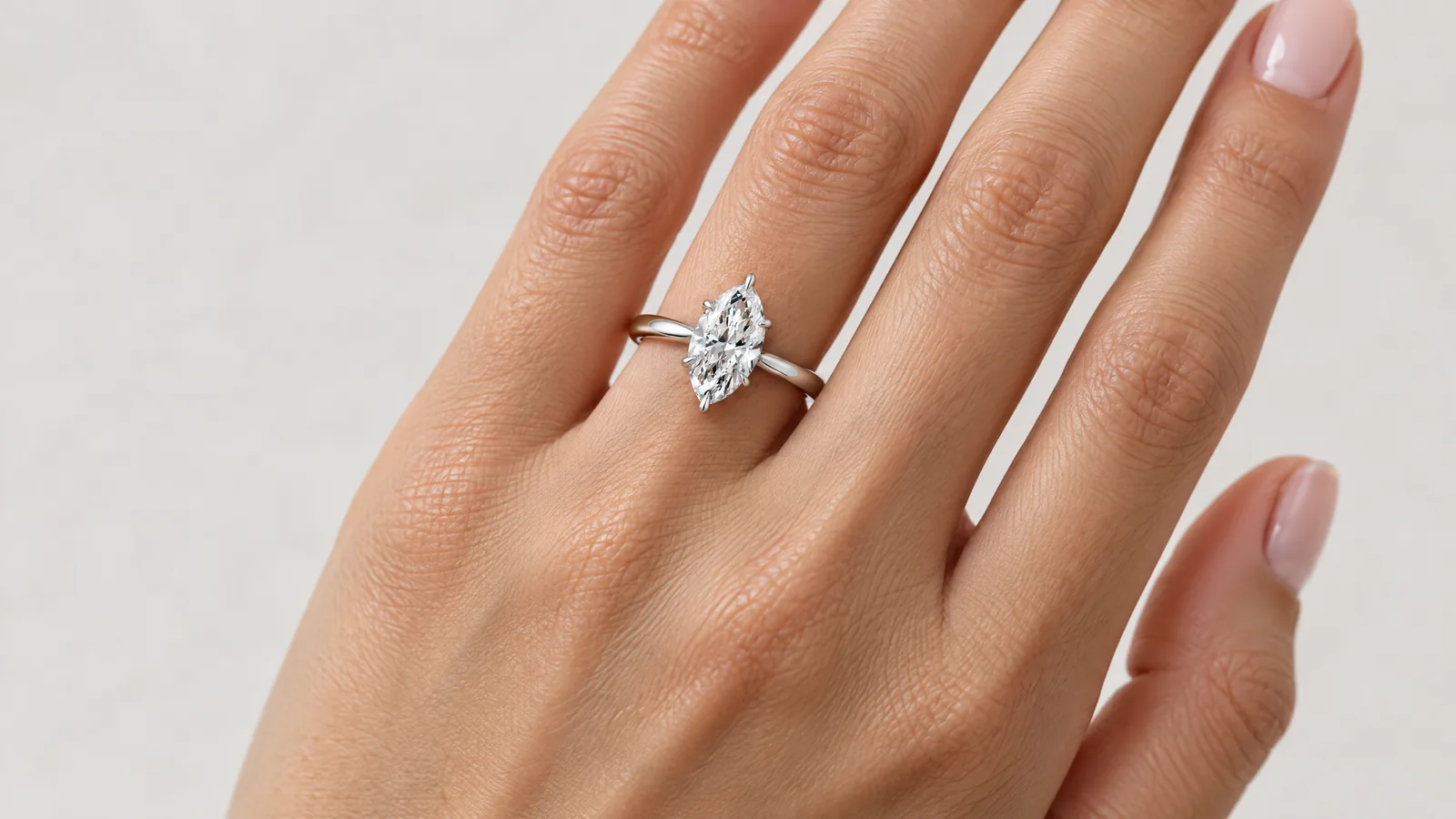 The back of a hand with the fingers slightly spread, wearing a white gold marquise diamond solitaire on the ring finger