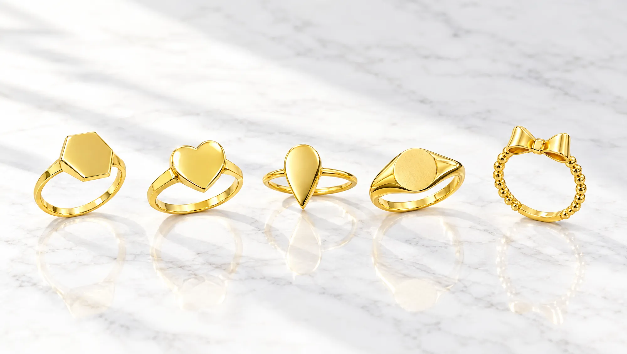Five 18K gold Mazimo signet rings on white marble