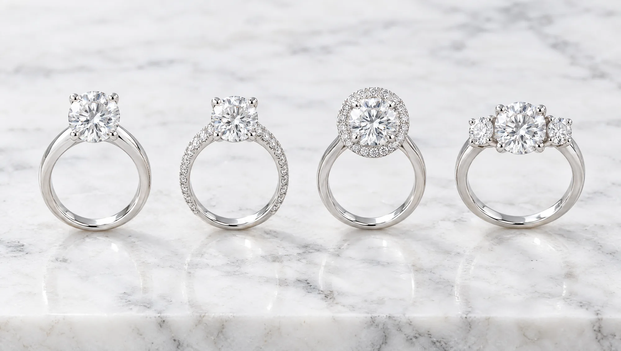 Four white gold engagement rings in a row: a solitaire, a pavé band, a halo and a three-stone ring