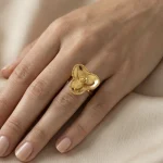 21K gold flower design ring with textured details on a model hand and white background